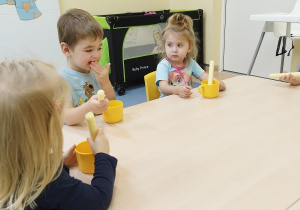 dzieci siedzą przy stoliku , trzymaja chrupkę i kubek z miodem