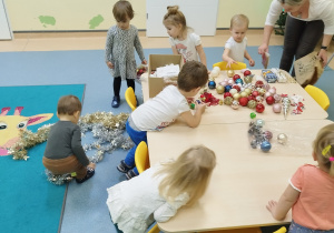 dzieci i ciocie wybierają rozsypane na stoliku ozdoby na choinkę