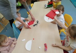 opiekunka pomaga dziewczynce w przyklejeniu elementów, druga dziewczynka wymachuje gotową pracą
