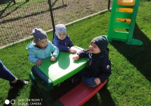 dzieci siedzą na ławeczkach przy stoliku