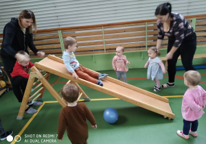 chłopiec zjeżdża z drewnianej zjeżdżalni, dzieci chodzą dookoła