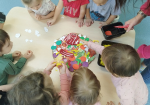 dzieci dokładają papierowe dodatki na pizze z kartonu
