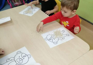 dzieci siedzą przy stoliku i wykonują pracę plastyczną