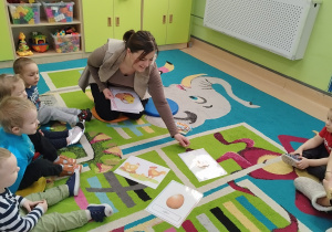 opiekunka opowiada dzieciom siedzącym na dywanie o jajku i kurce