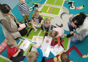 dzieci na dywanie oglądają ilustracje o kurkach i jajku