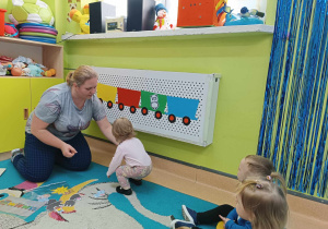 dziewczynka wraz z opiekunką siedzą obok grzejnika z przyklejonym pociągiem