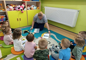 opiekunka pokazuje dzieciom siedzącym na dywanie ilustracje pociągów
