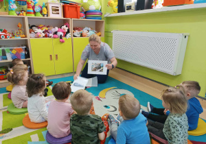 dzieci siedzą, a opiekunka pokazuje im ilustracje dawnych pociągów