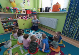 dzieci siedzą na dywanie słuchają wiersza czytanego przez opiekunkę