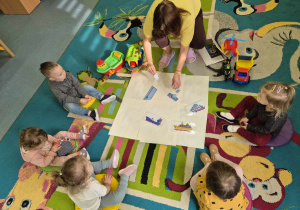 opiekunka przygotowuje na dywanie rozsypankę obrazkową