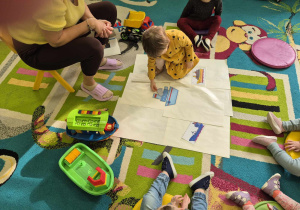 dziewczynka układa z rozsypanych elementów statek, a dzieci się przyglądają