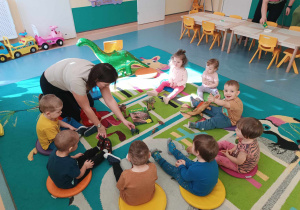 dzieci siedzą na dywanie i opiekunka pokazuje im różne figurki dinozaurów