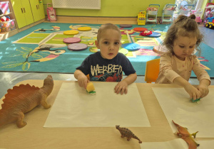 dzieci siedzą przy stoliku i malują gąbkami z farbą gipsowe dinozaury