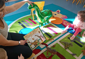 opiekunka czyta dzieciom książkę o dinozaurach