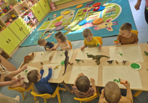 dzieci siedzą przy stoliku i malują gipsowe figurki dinozaura