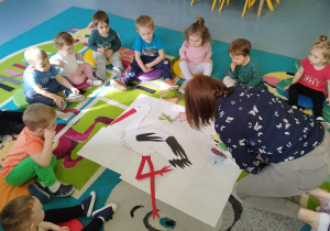 dzieci siedzą na dywanie wkoło rozłożonych ilustracji zwierząt, które układa opiekunka