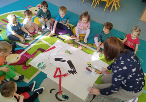 dzieci wraz z opiekunką oglądają ilustracje zwierząt