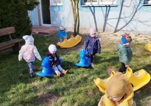 dzieci chodzą po trawie, siedzą i wsiadają na bujaki