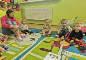dzieci z opiekunką siedzą na dywanie