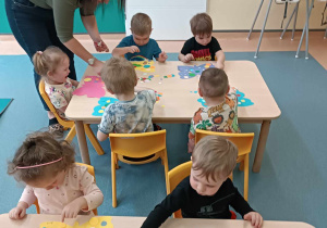opiekunka pomaga dzieciom siedzącym przy stoliku wyklejać papierowe motyle