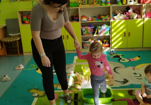 opiekunka trzyma dziewczynkę za ręke i pomaga jej przejść po ścieżce
