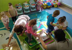 dzieci siedzą z opiekunkami wokół ścieżki, a dziecko po niej idzie