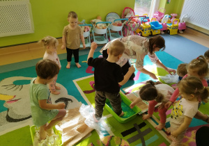 chłopiec wchodzi stopą do pudełka z kulkami, dzieci stoją i siedzą wokół
