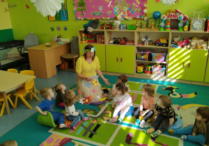 dzieci wraz z opiekunkami siedzą i słuchają czytanego wiersza
