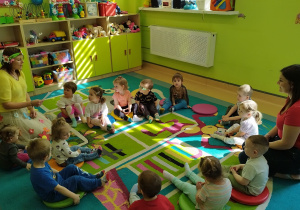 dzieci wraz z opiekunkami siedzą na dywanie, słuchają wiersza