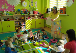 pani wiosna rozrzuca kwiaty dzieciom siedzącym na dywanie