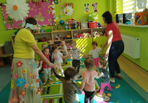 dzieci wraz z opiekunkami trzymajać się za ręce tańczą w koło