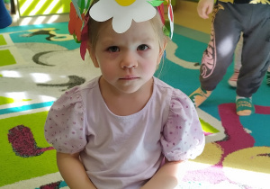dziewczynka siedzi na podłodze na głowie ma wianek z dużym kwiatkiem