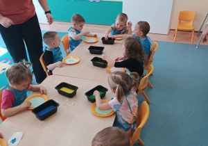 dzieci siedzą przy stoliku, maczają patyczki w farbie i wykonują pracę
