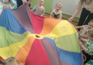 dzieci wraz z opiekunkami trzymają chustę, tańczą