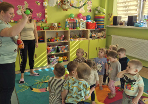 dzieci stoją na kolorowej chuście, opiekunka pokazuje kolor piłeczki