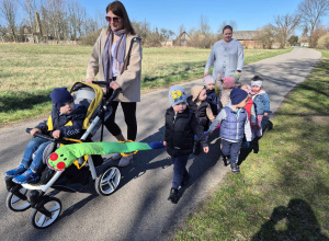 opiekunka pcha wózek za nią maszerują dzieci wraz z opiekunką