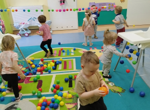 na podłodze dużo kolorowych piłek, dzieci je zbierają