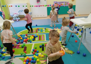 dużo kolorowych piłek na podłodze, dzieci je zbierają