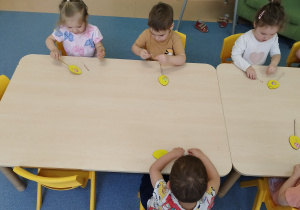 dzieci przy stoliku przyklejają ozdoby do jajka