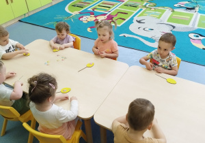 dzieci przy stoliku przyklejają ozdoby do jajka