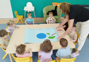 dzieci siedzą przy stoliku, na którym leży karton i elementy planety