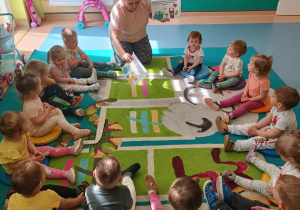 dzieci siedzą na dywanie , opiekunka pokazuje plansze