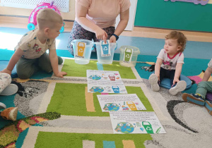 opiekunka pokazuje wiaderka z naklejonym kolorem kosza i informacją, co do niego wrzucamy