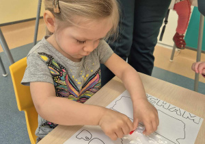 dziewczynka przykleja bibułę do kartki posmarowanej klejem