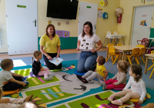 dzieci wraz z opiekunkami siedza na dywanie, opiekunka pokazuje bluzkę na której ma narysowane pszczoły
