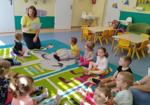 wszyscy siedzą na dywanie i słuchają czytanego przez opiekunkę wiersza