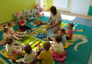dzieci siedzą na dywanie , niektóre mają łyżeczki z miodem, opiekunka patrzy