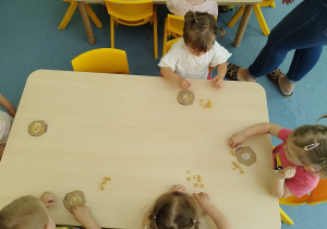 dzieci przy stoliku przyklejają makaron do tekturek