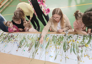 dzieci i rodzice przyklejają do kartonu trawy i kwiaty