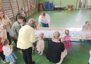 dzieci i rodzice wokół kartonu przyklejają trawy i kwiaty
